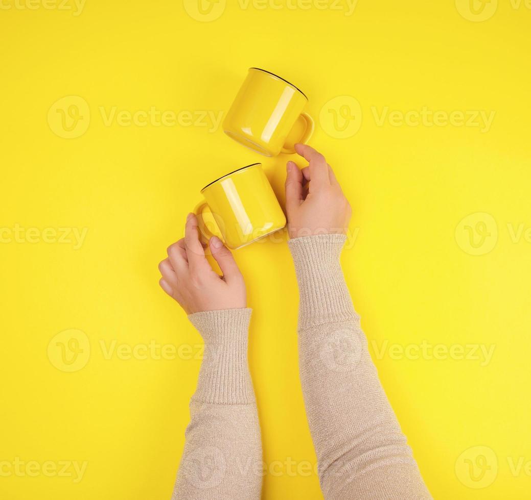 Zwei gelbe Keramikbecher werden von einer weiblichen Hand getragen foto