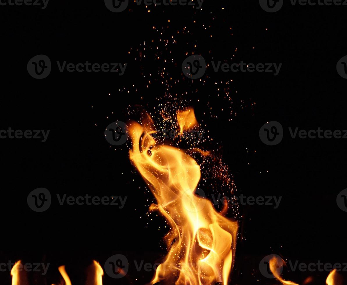 großes brennendes Lagerfeuer mit Flamme und orangefarbenen Funken, die in verschiedene Richtungen fliegen foto