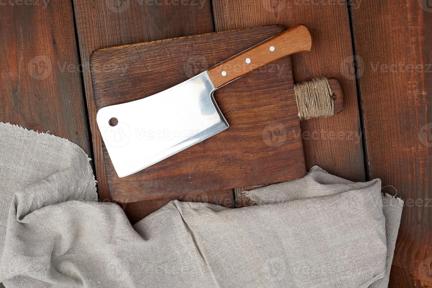 Ein großes scharfes Fleischmesser aus Stahl liegt auf einem rechteckigen braunen Holzbrett foto