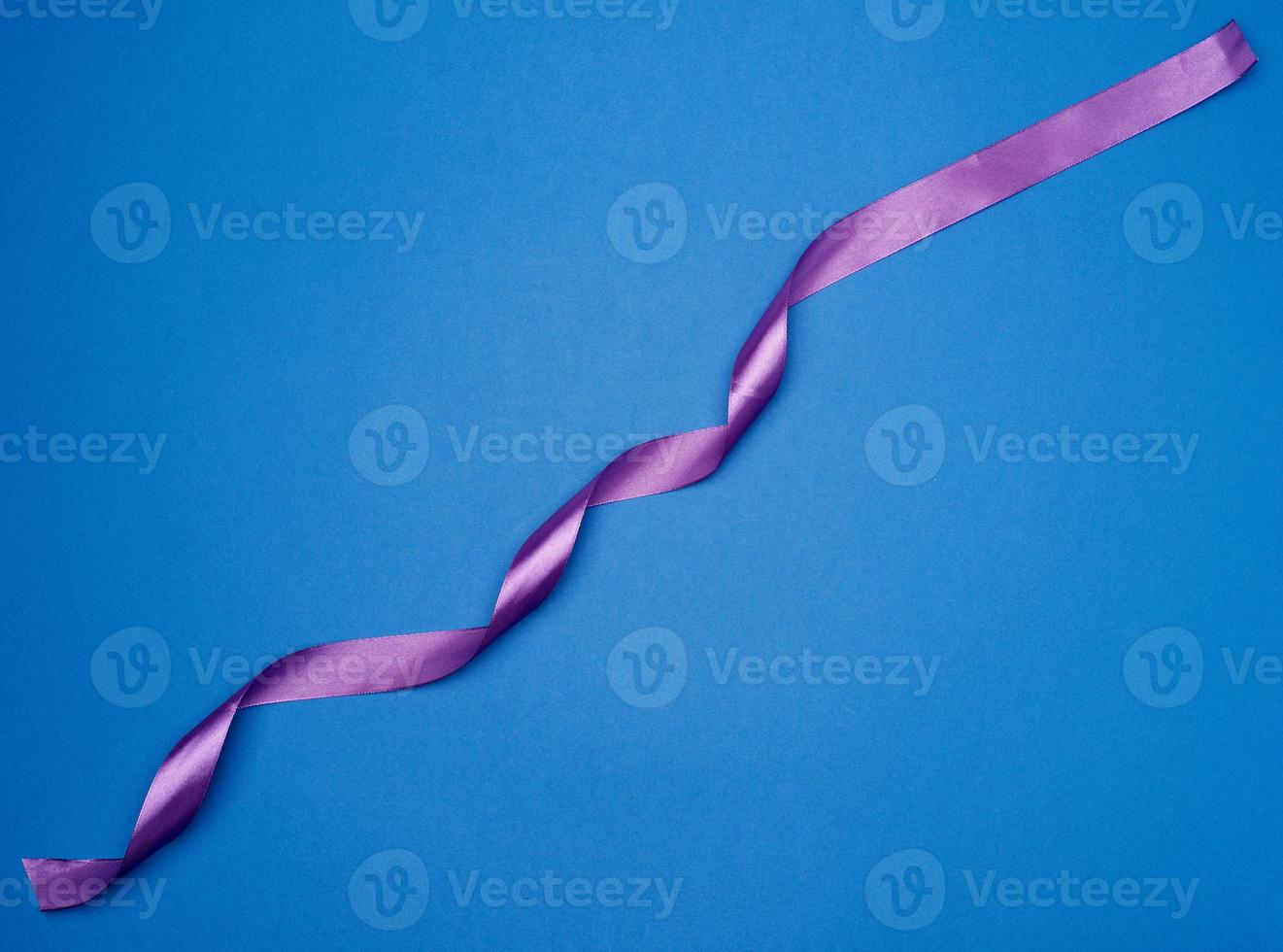 violettes dünnes Seidenband, das auf blauem Hintergrund verdreht ist foto