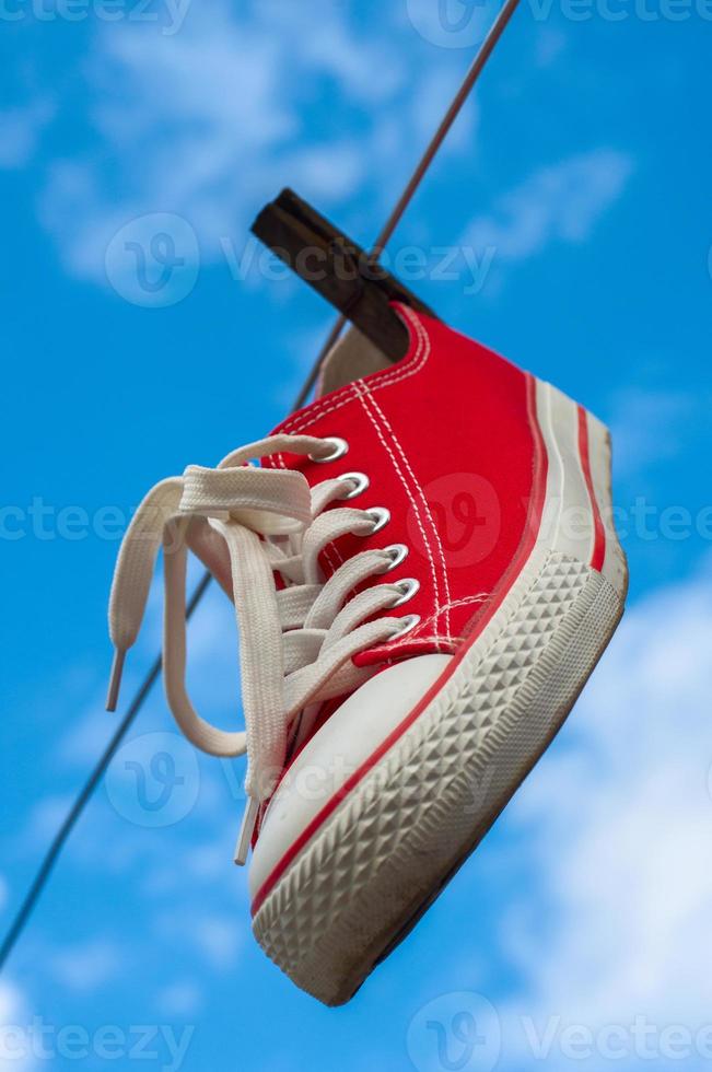 ein roter Turnschuh, der an einer Wäscheleine vor blauem Himmel hängt foto