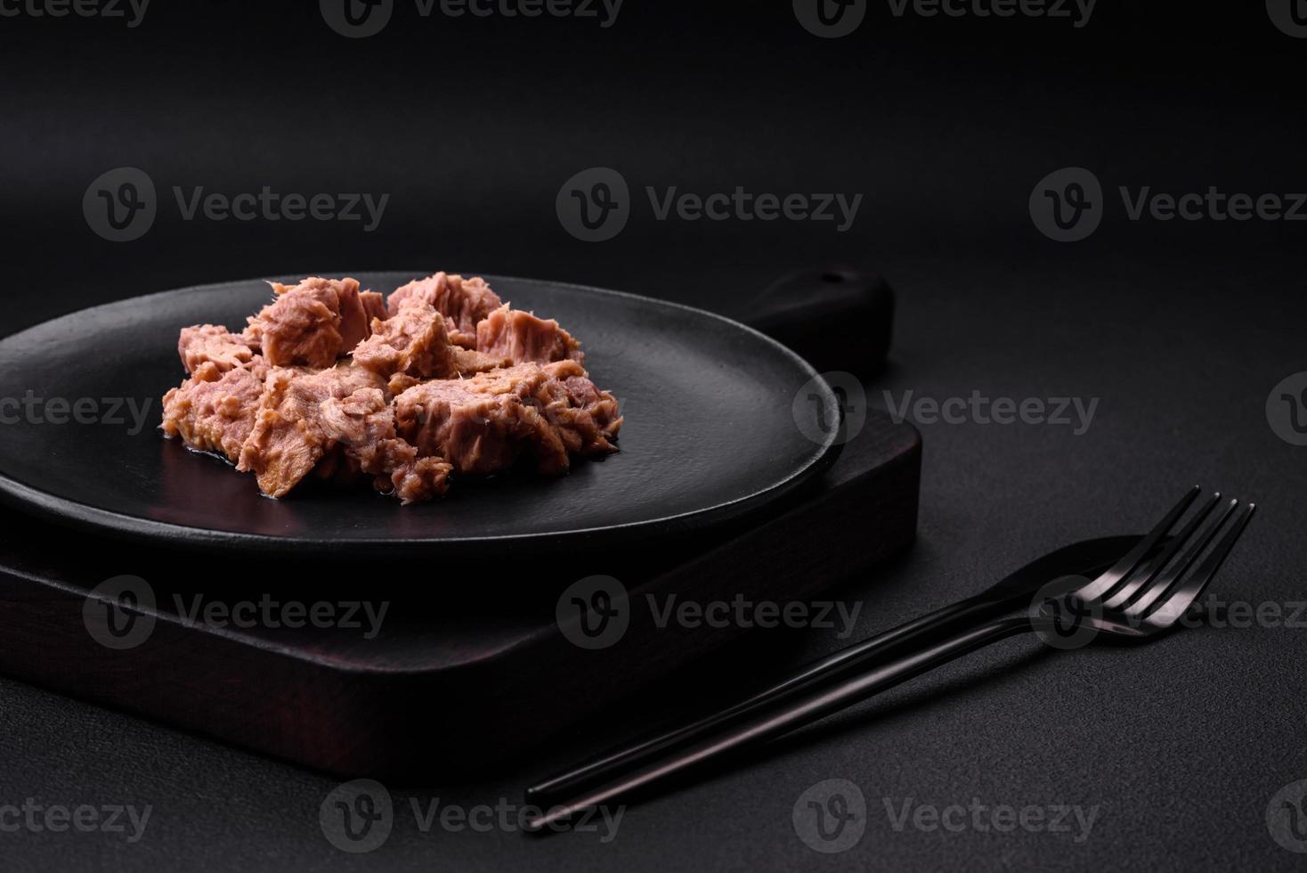 Köstliches Thunfischfleisch in Dosen auf einer schwarzen Keramikplatte auf dunklem Betonhintergrund foto