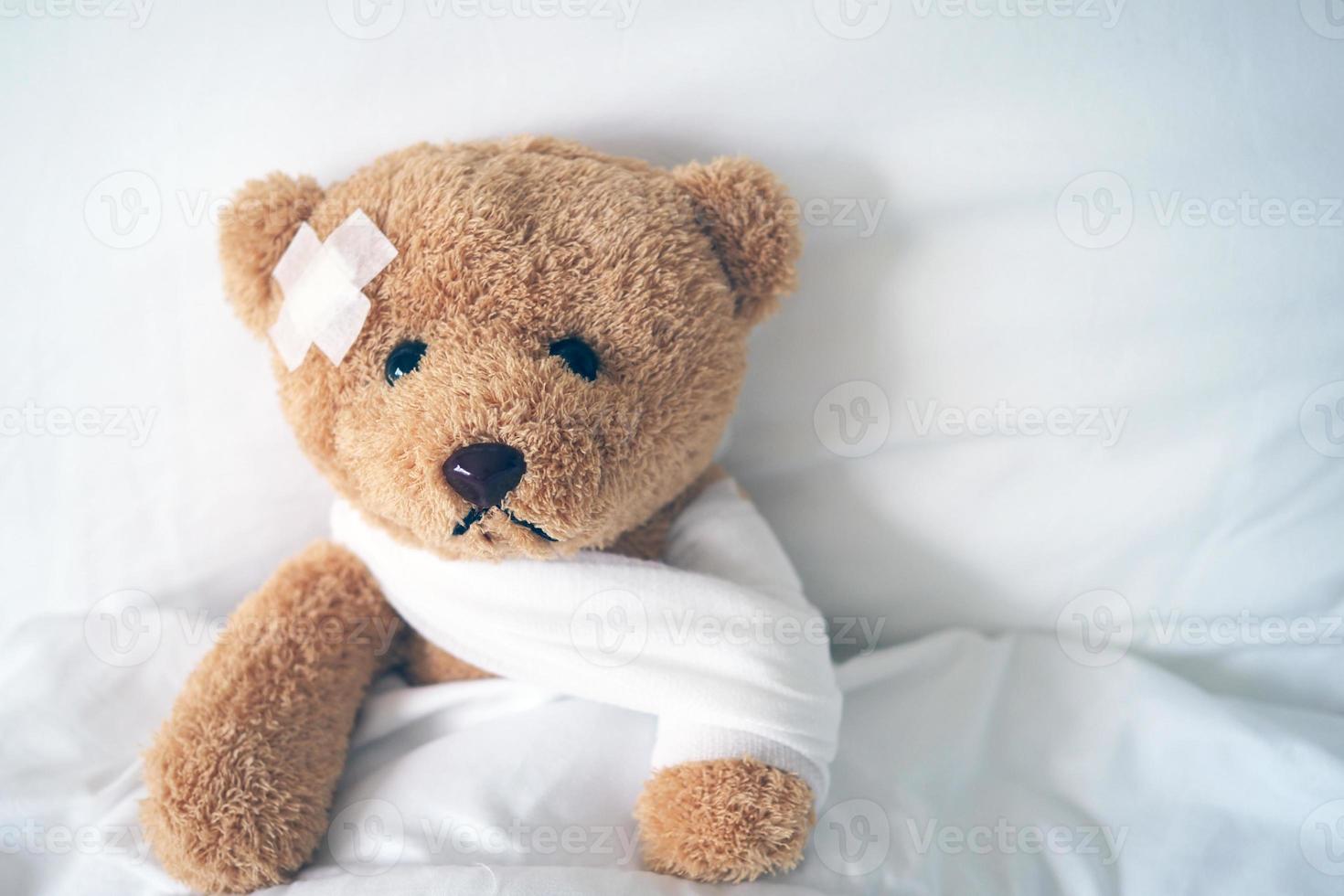 teddybär liegt krank im bett mit einem stirnband und einem tuch bedeckt foto