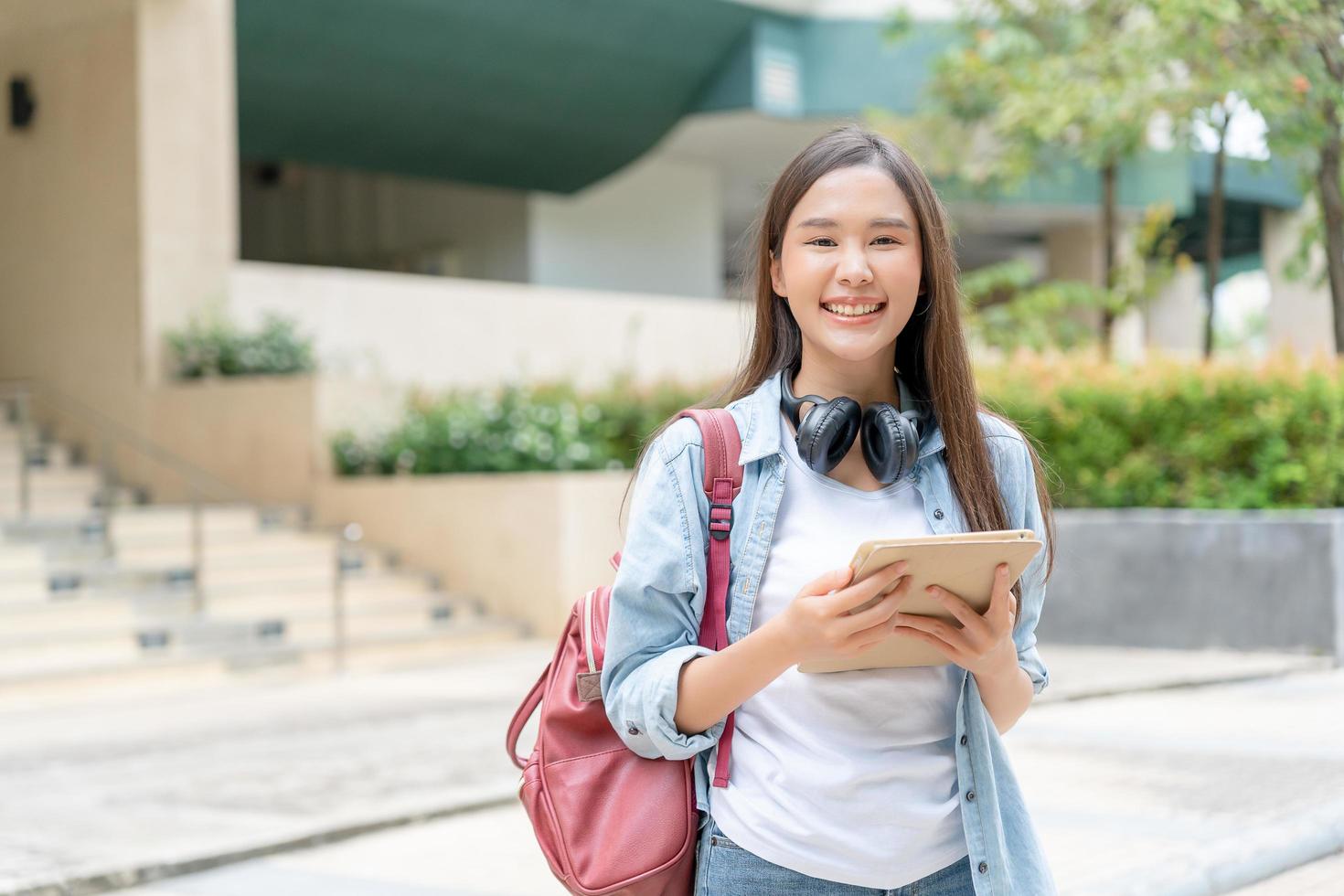 schöne asiatische Studentin mit Rucksack und Büchern im Freien. lächelndes Mädchen, das glücklich ist, viel Buch auf dem College-Campus zu tragen. Porträtfrau an der International Asia University. Bildung, Studium, Schule foto