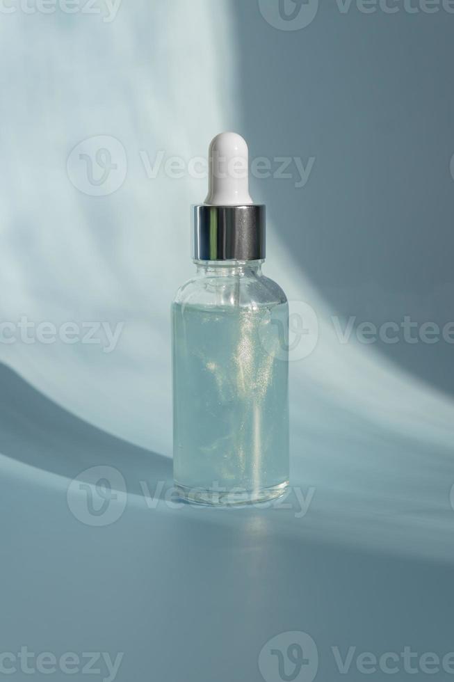 Kosmetik-Spa medizinische Hautpflege, Glas-Serumflasche mit Meereskollagen auf blauem Hintergrund mit Sonnenschatten. Präsentation von kosmetischen Produkten ohne Markenzeichen. Platz kopieren foto