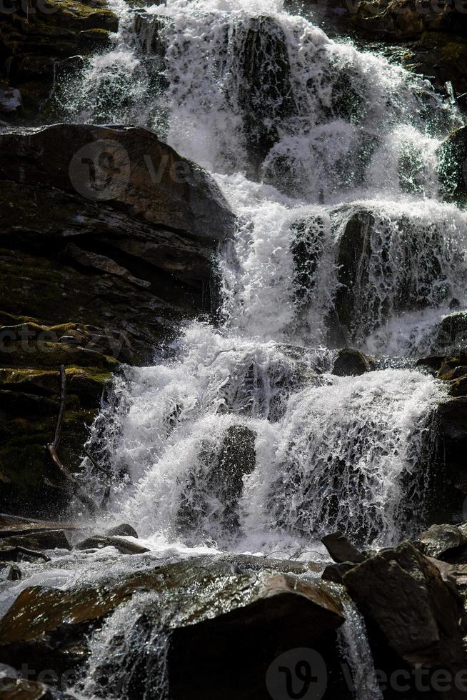 Das Wasser fließt einen kleinen Bergbach hinunter und fließt über Basaltblöcke. ein kleiner Wasserfall fließt durch das Moos. foto