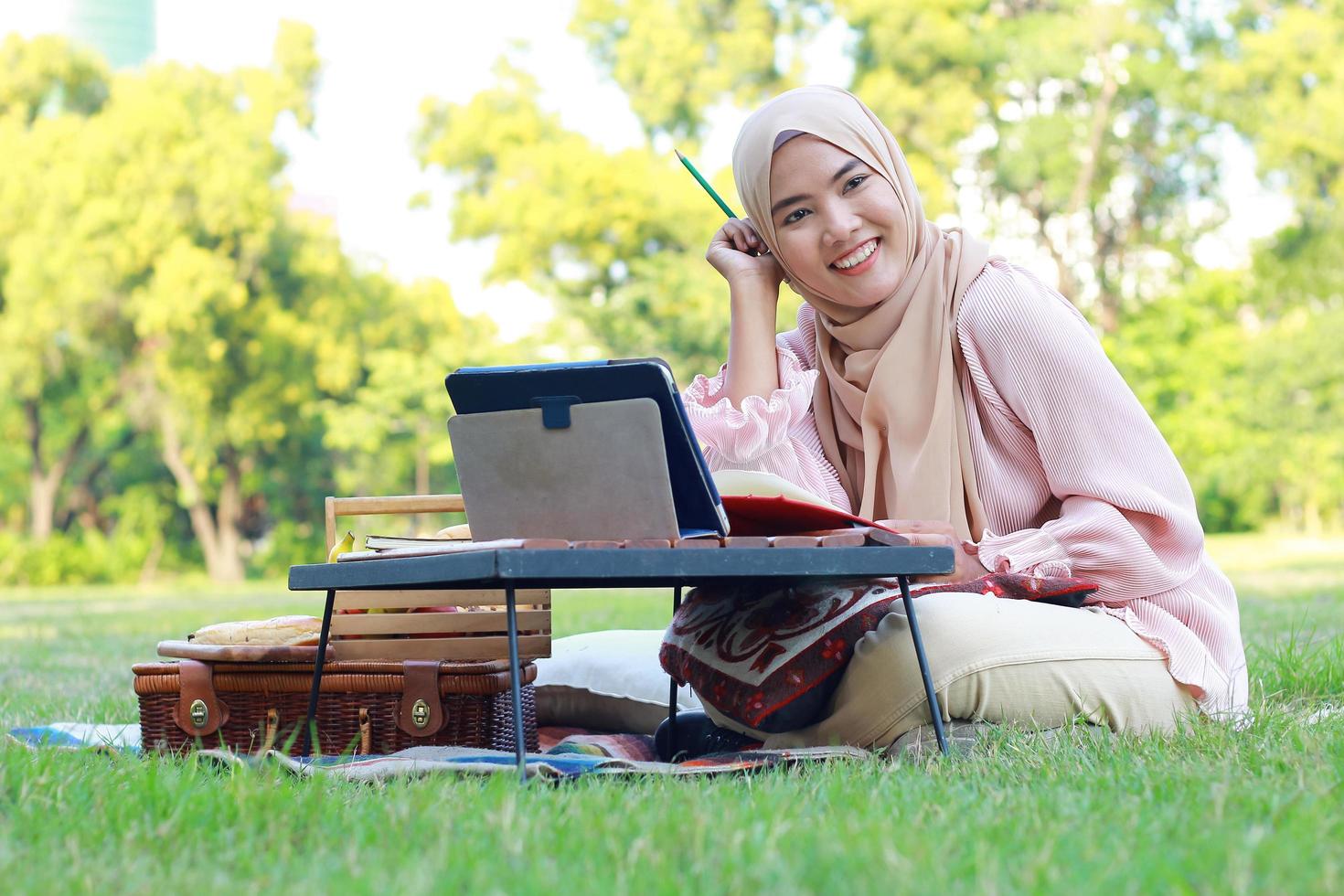 schönes muslimisches Mädchen, das glücklich im Park sitzt. muslimische Frau, die im Gartenrasen lächelt. Lebensstilkonzept einer selbstbewussten modernen Frau foto