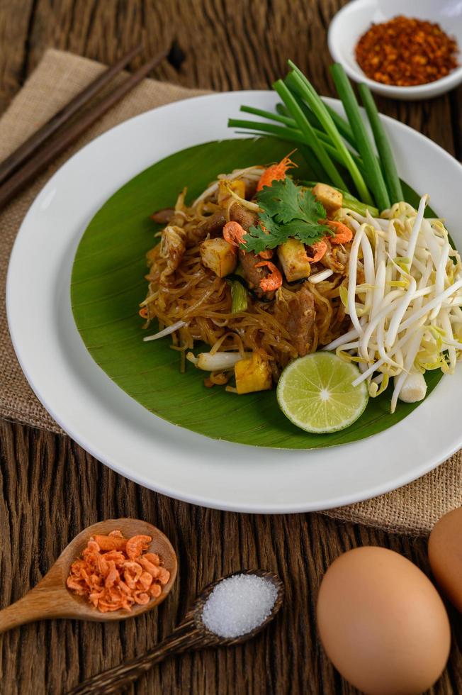 Pad Thai mit Zitrone, Eiern und Gewürzen auf einem Holztisch foto