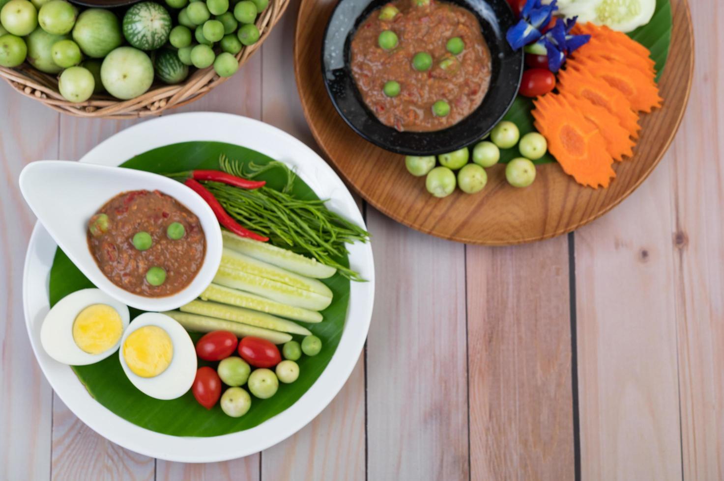 Chilipastenpaste in einer Schüssel mit Auberginen, Karotten, Chili und Gurken in einem Korb foto