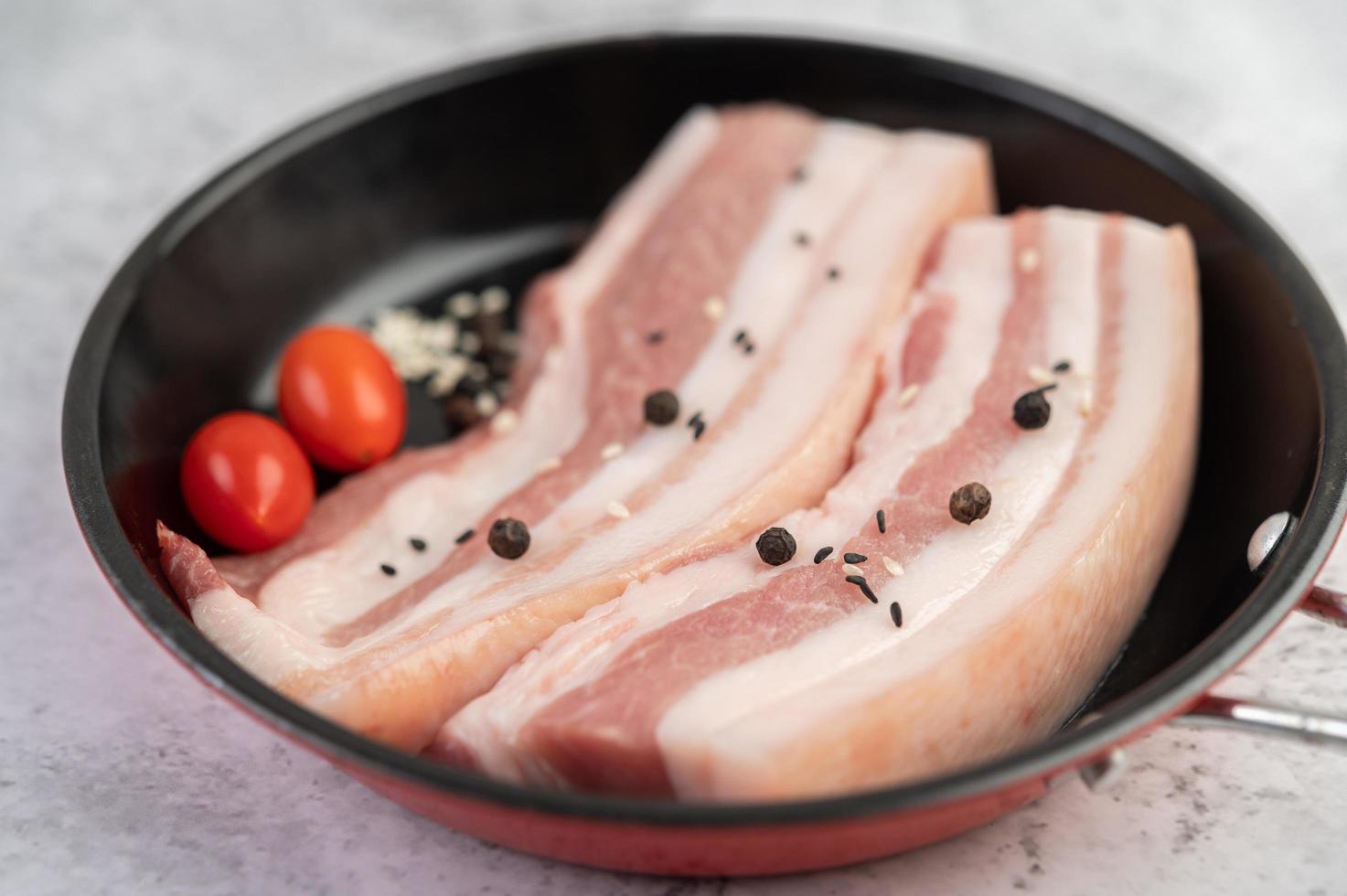 Schweinebauch in einer Pfanne mit Pfeffersamen, Tomaten und Gewürzen foto