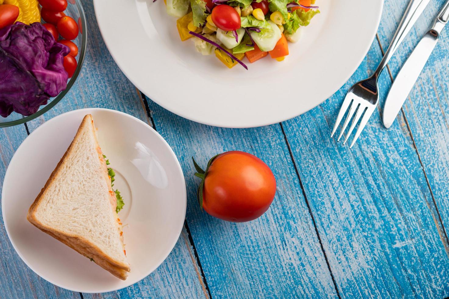 frischer Salat auf einem weißen Teller mit Sandwich und Tomaten foto