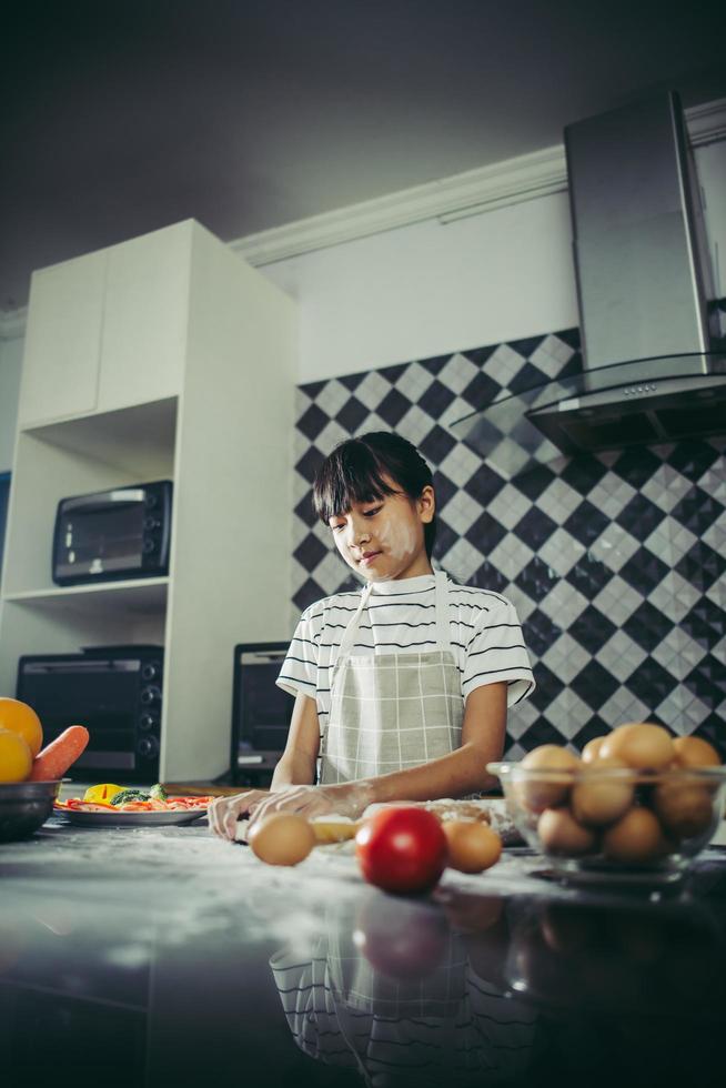 süßes kleines Mädchen knetet Mehlteig in der Küche foto