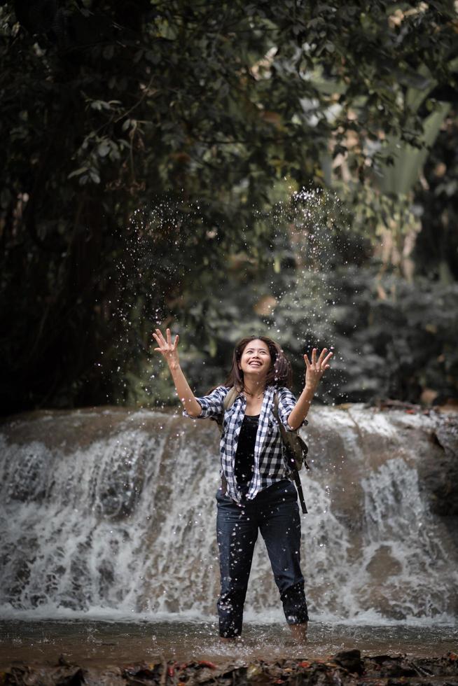 junge Frau, die Spaß unter einem Wasserfall im Wald hat foto