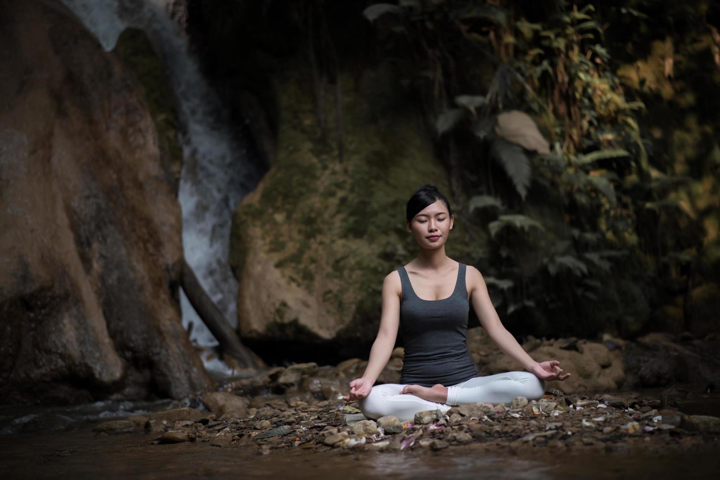 junge Frau in einer Yoga-Pose, die nahe einem Wasserfall sitzt foto