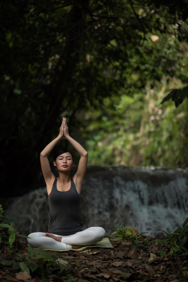 junge Frau in einer Yoga-Pose, die nahe einem Wasserfall sitzt foto