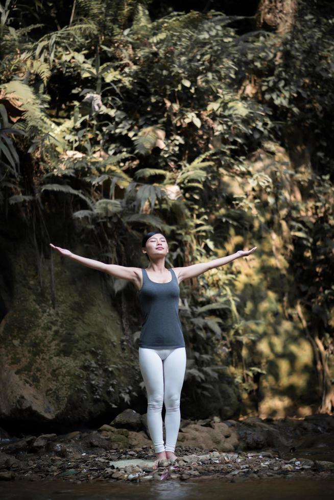 junge Frau in einer Yoga-Pose nahe einem Wasserfall foto