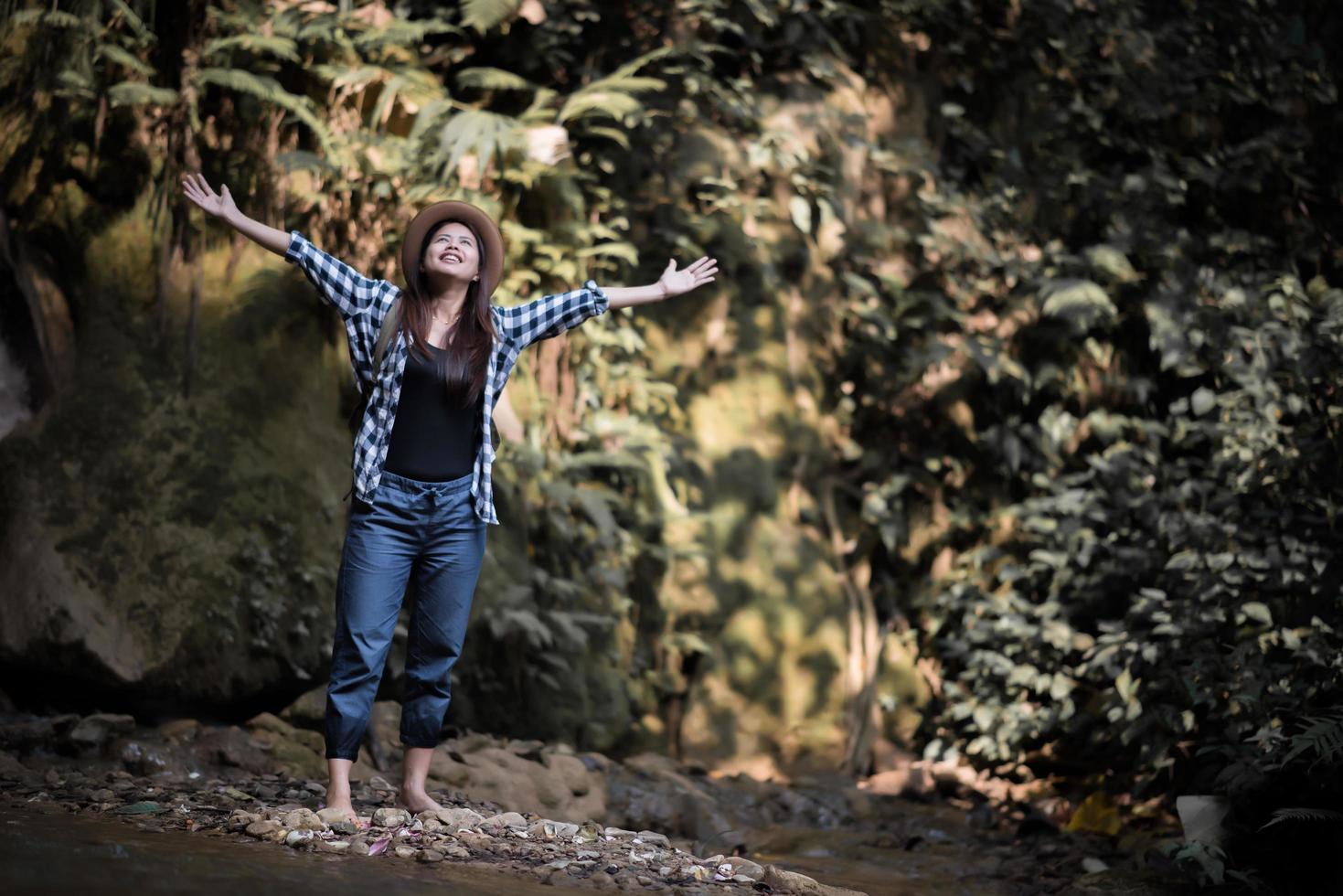 glückliche junge Frau, die ihre Arme hebt, um die Sonne im Wald zu begrüßen foto