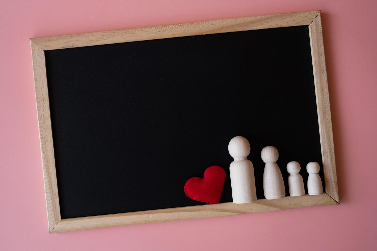 holzfiguren von familienvater, mutter und kindern auf der schwarzen tafel auf rosa hintergrund. Platz für Text kopieren. foto