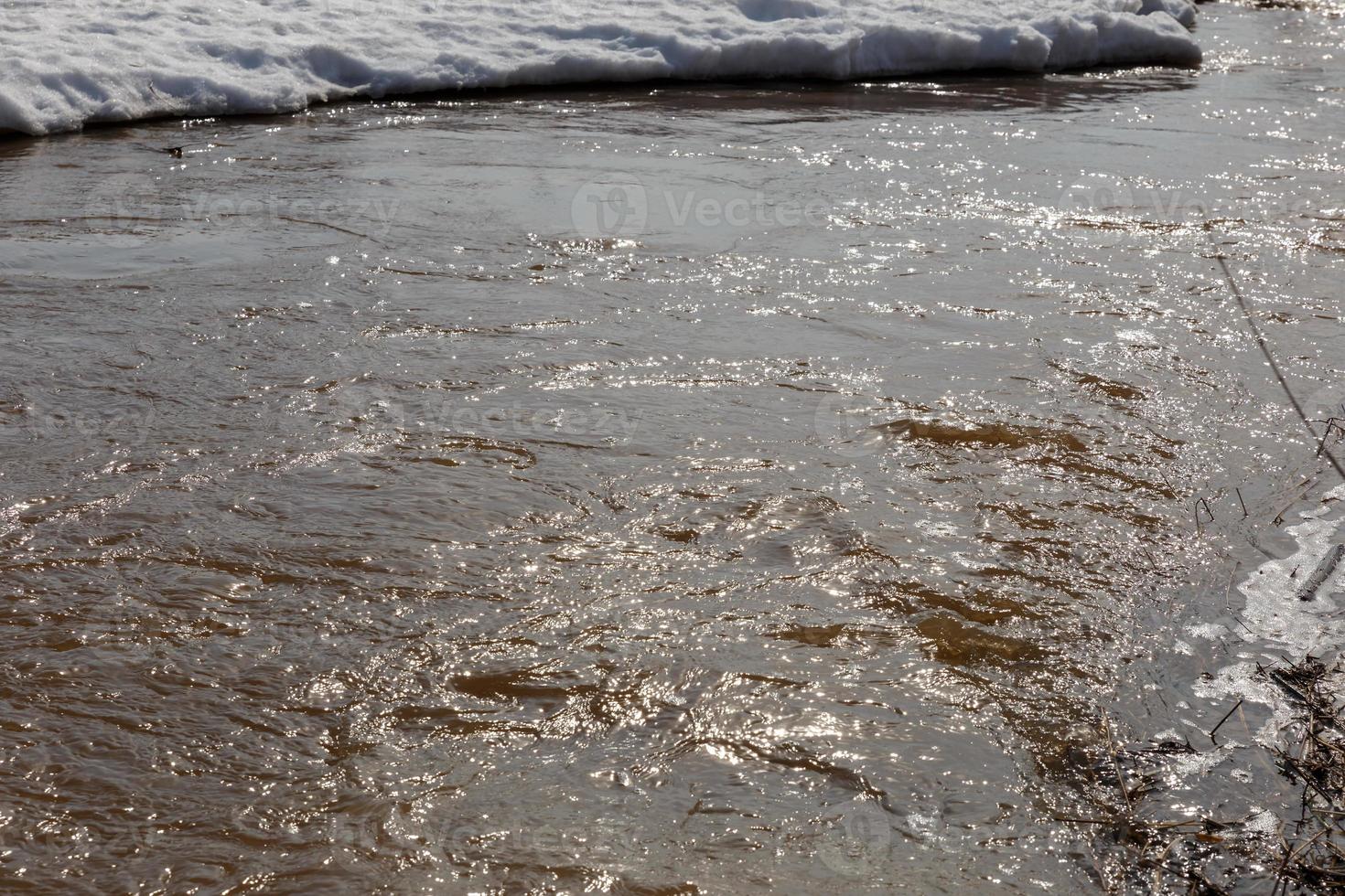 Sonnenlicht, das sich im Wasser spiegelt. Frühling schmelzender Schnee. Flusswasserkräuselungen, die mit Sonnenlicht glänzen. foto