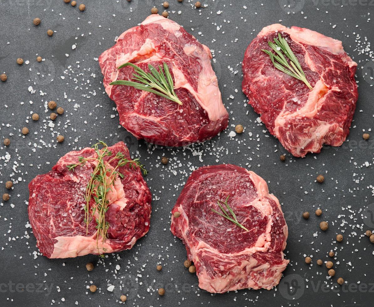 rohes Stück Rindfleisch Ribeye mit Rosmarin, Thymian auf einem schwarzen Tisch, foto