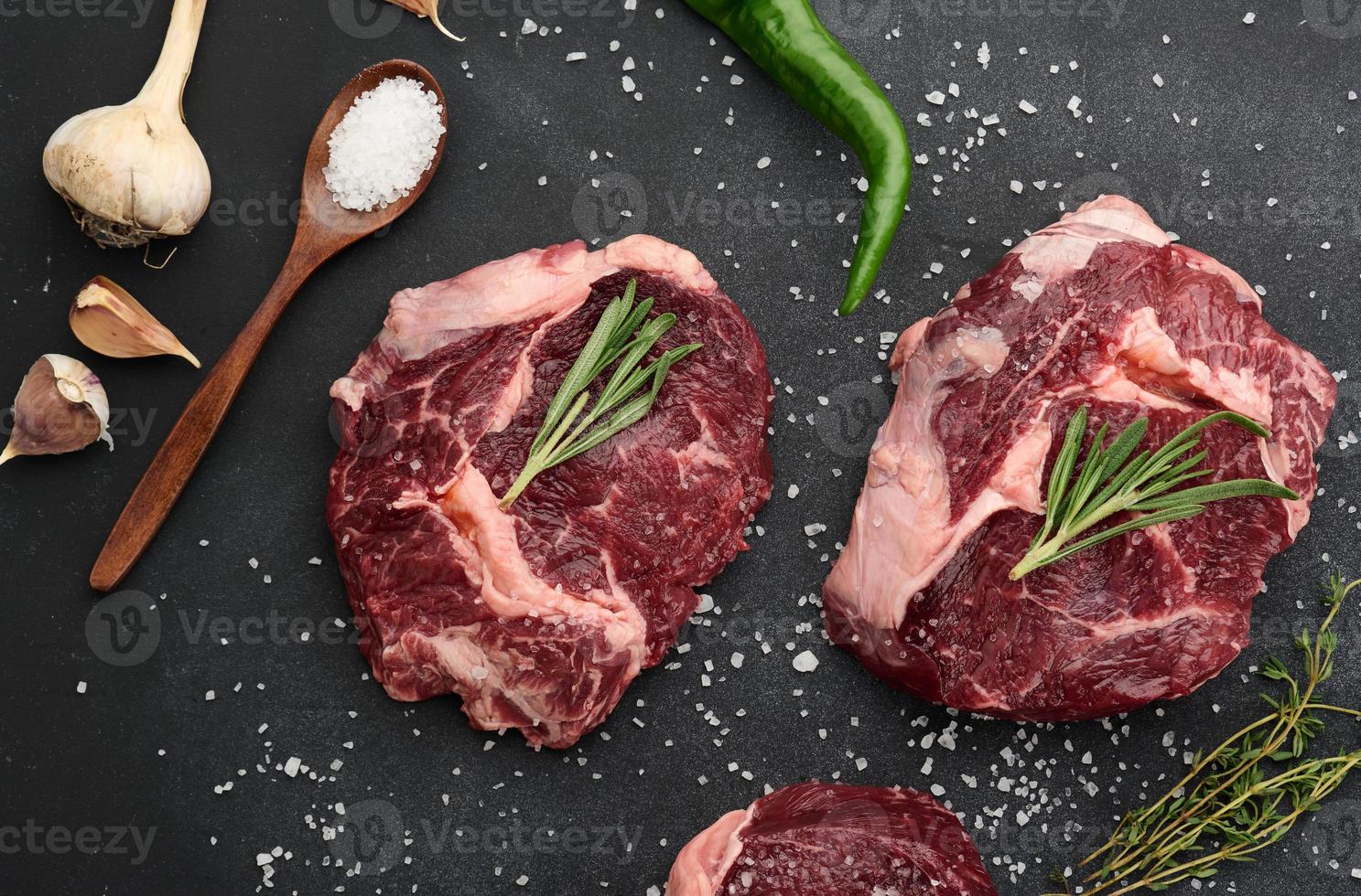 Rohes Stück Rindfleisch Ribeye mit Rosmarin, Thymian auf einem schwarzen Tisch, Draufsicht foto