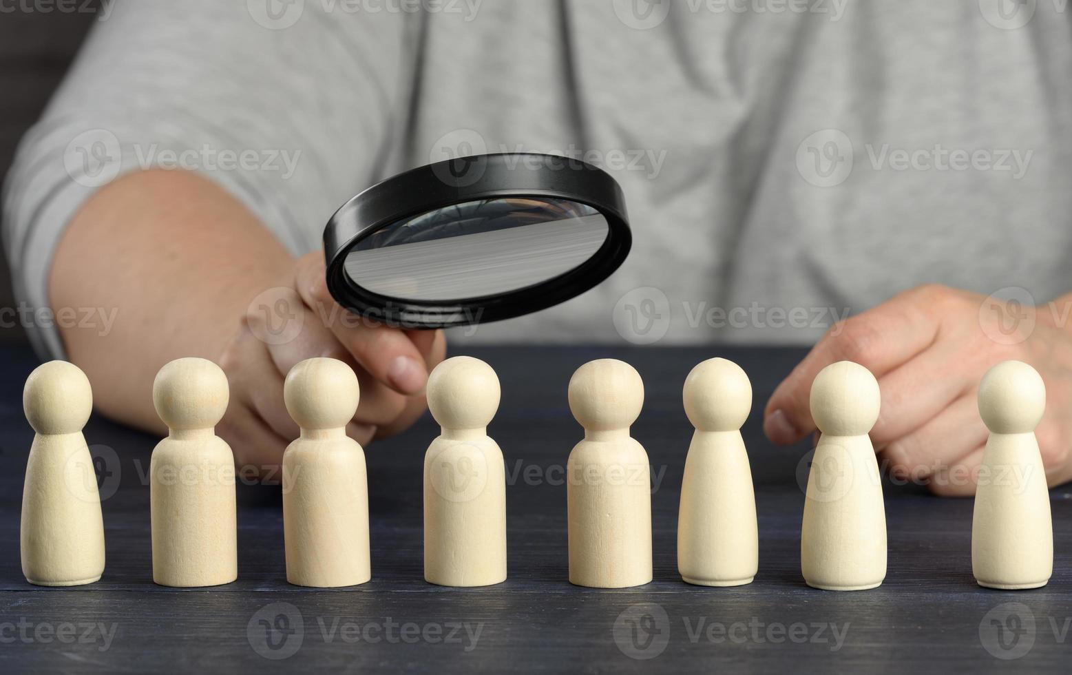 Eine Hand mit einer Lupe untersucht einzigartige und talentierte Holzmänner in der Menge. mitarbeitersuchkonzept, karrierewachstum foto