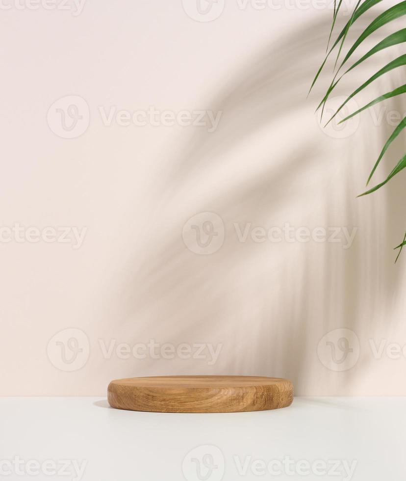 Bühne für die Präsentation von Produkten, Kosmetika mit einem runden Holzpodium und einem grünen Palmblatt. Schatten auf dem Hintergrund foto