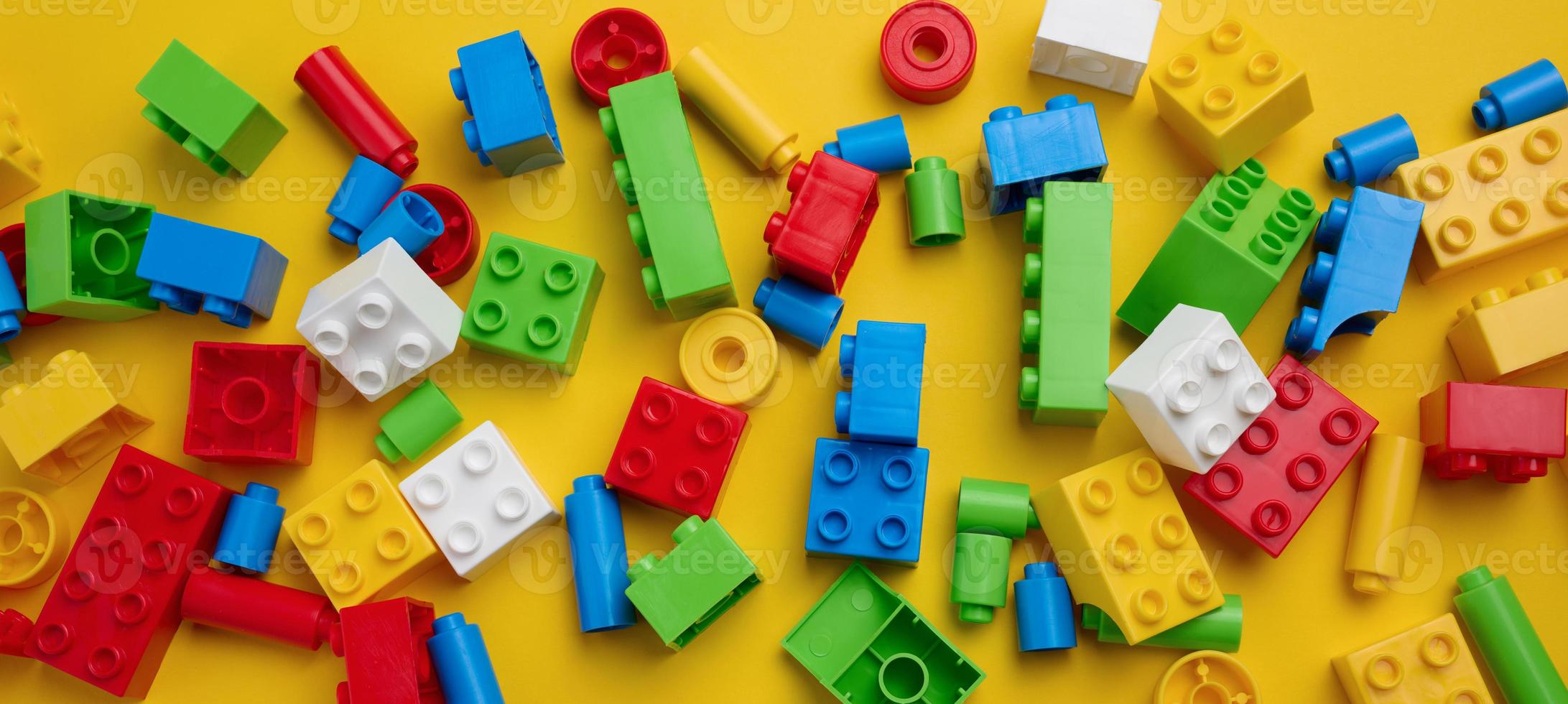 verstreute Teile eines Kinderdesigners aus Kunststoff, Ansicht von oben. gelber hintergrund, kopierraum foto