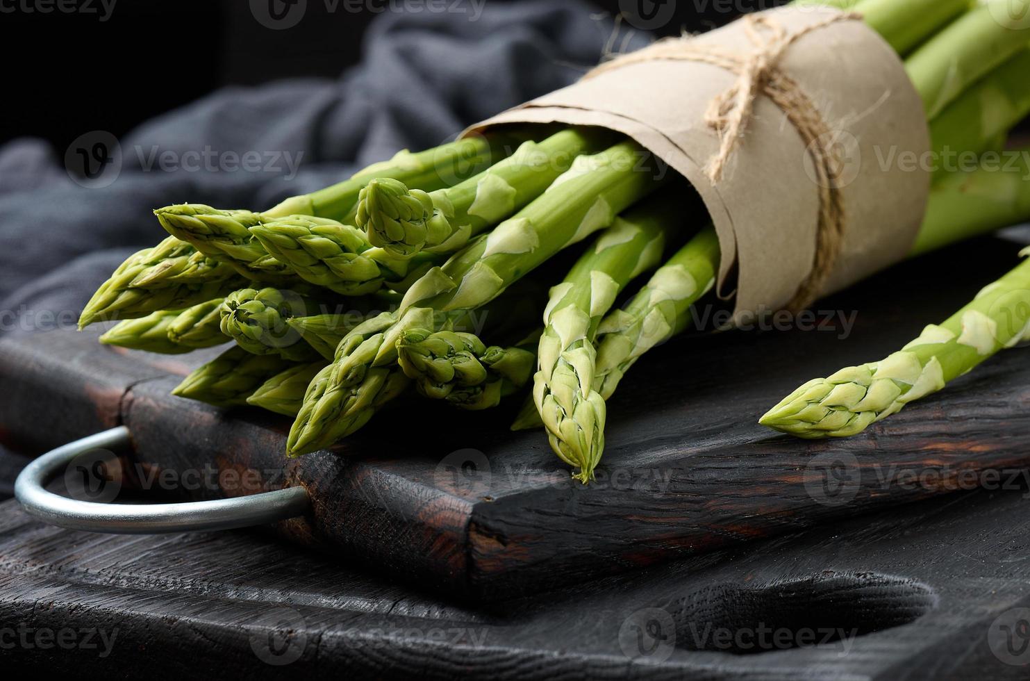 Bund frischer roher Spargel auf einem schwarzen Küchenbrett aus Holz foto