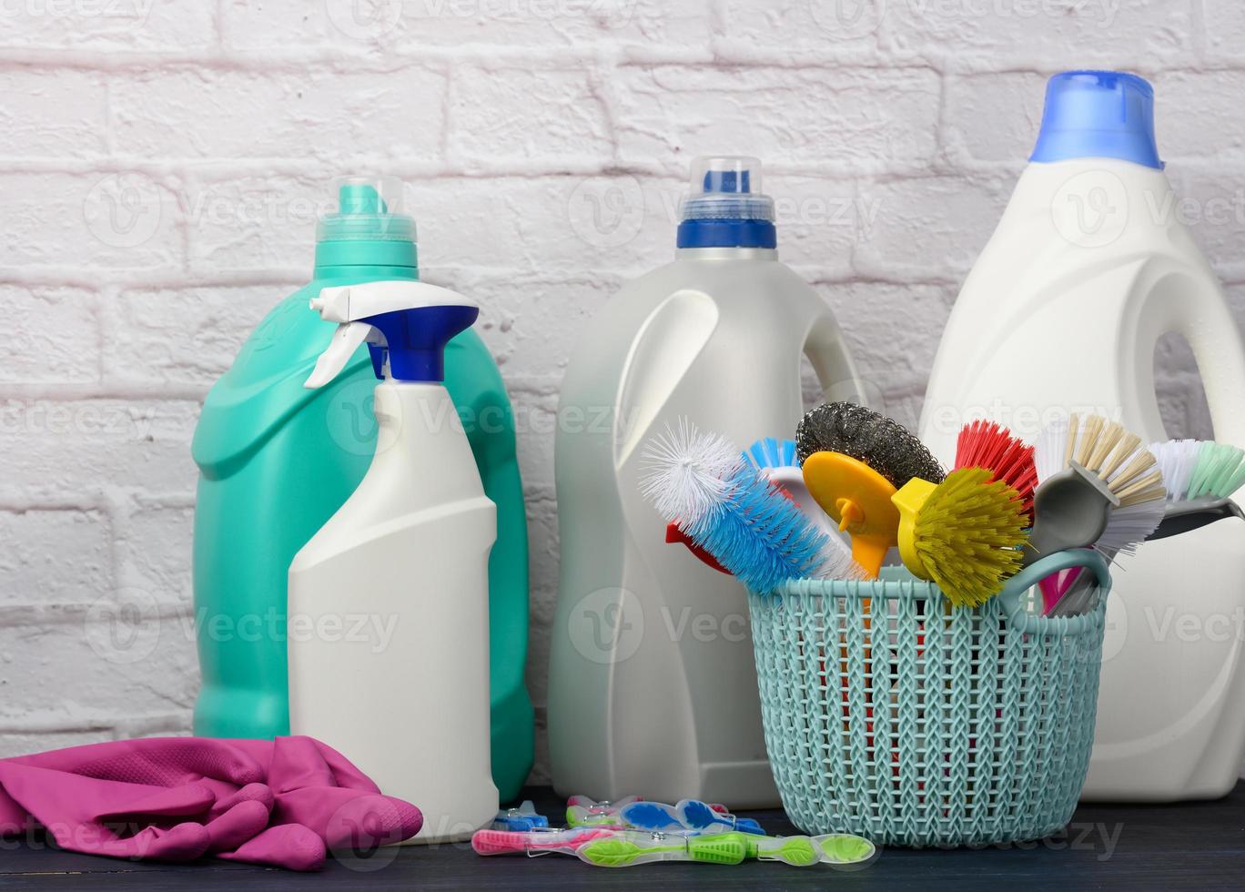 schwämme, plastikbürsten und waschmittelflaschen auf einem blauen holztisch. Haushaltsreinigungsartikel auf weißem Backsteinmauerhintergrund foto