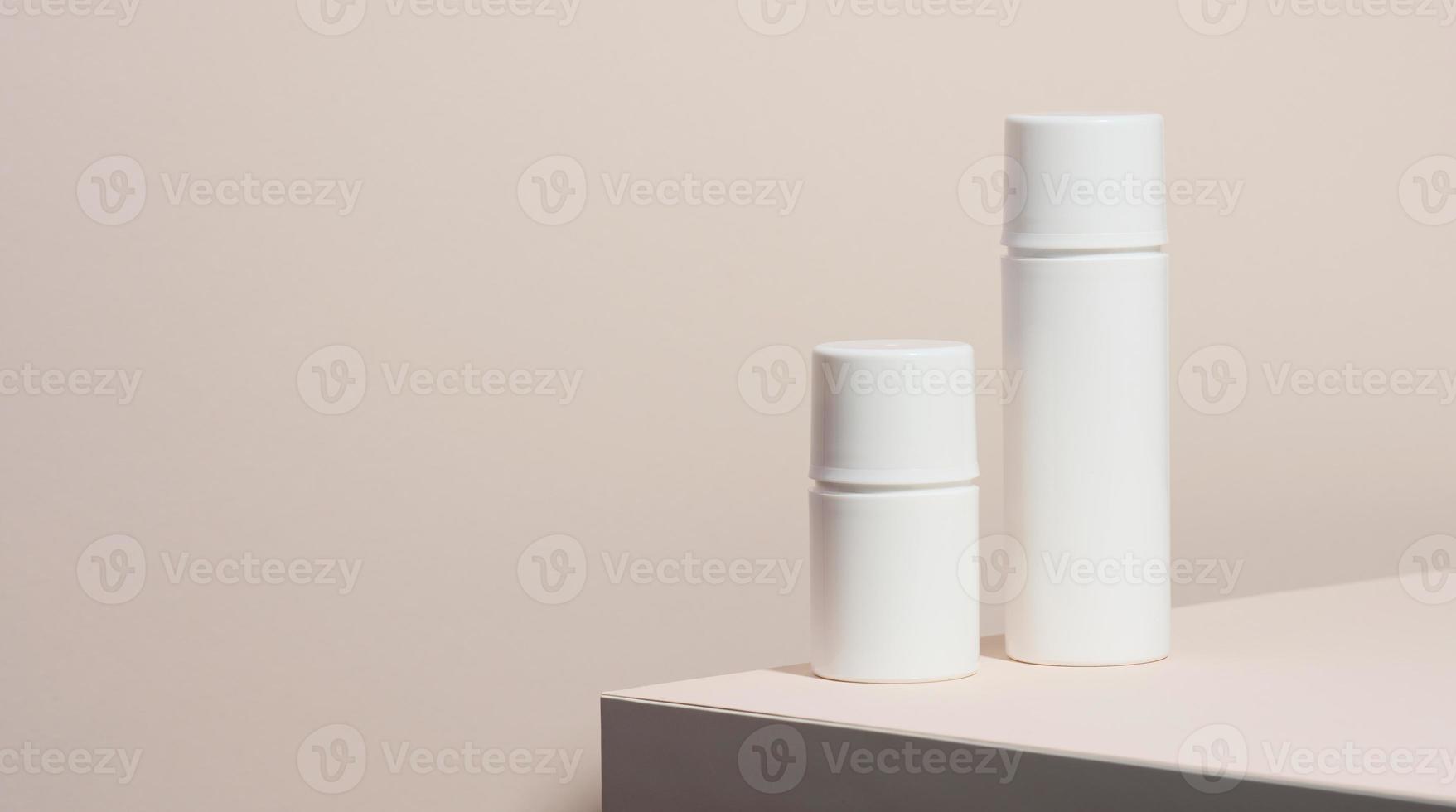 Leere weiße Kunststoffrohre für Kosmetika stehen auf einem Holzpodium auf beigem Hintergrund. Behälter für Cremes, Shampoos, flüssige Substanzen. Marke, Vorlage foto