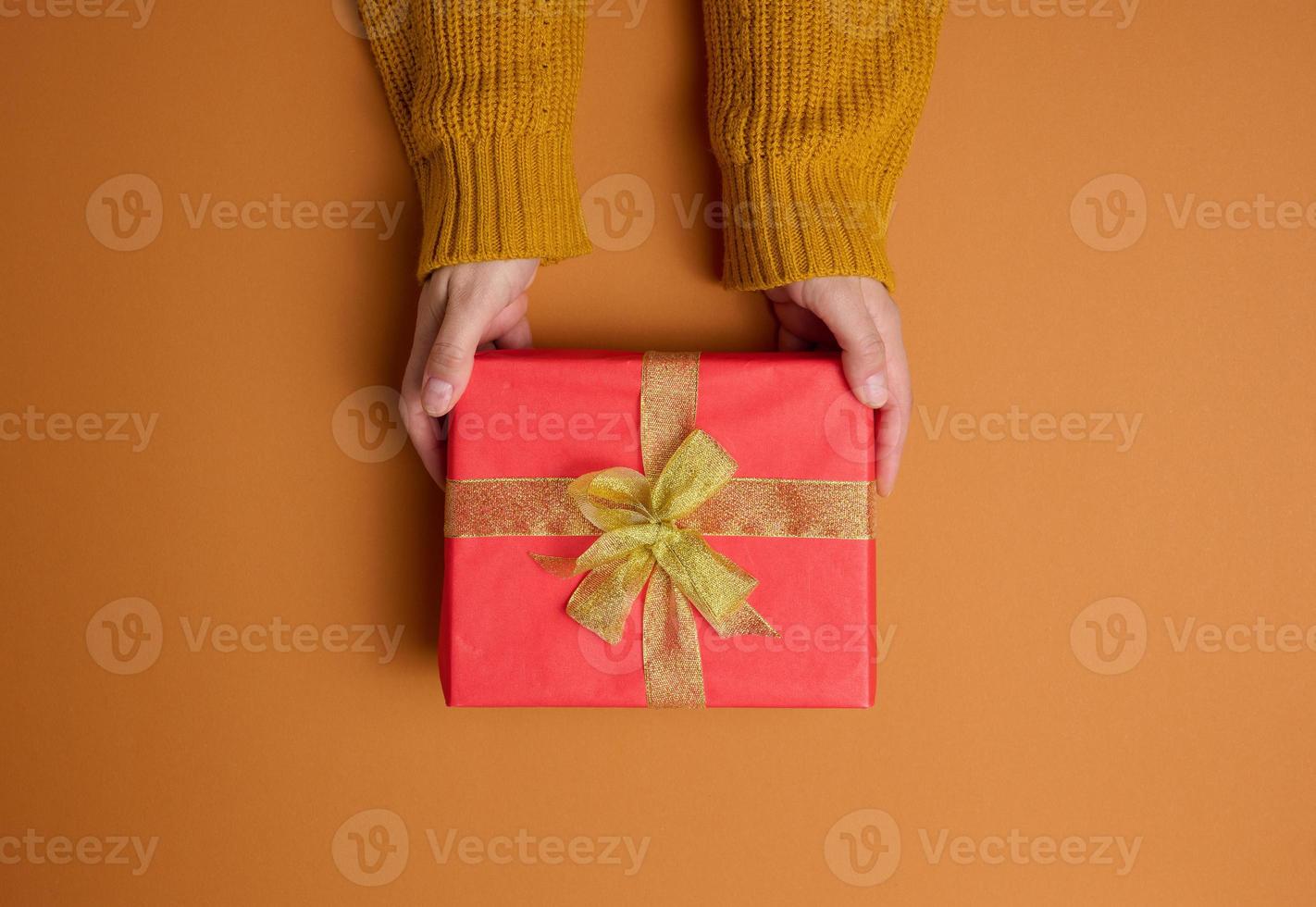 weibliche hände halten rote geschenkbox auf orangefarbenem hintergrund, konzept der glückwünsche zum geburtstag, draufsicht foto