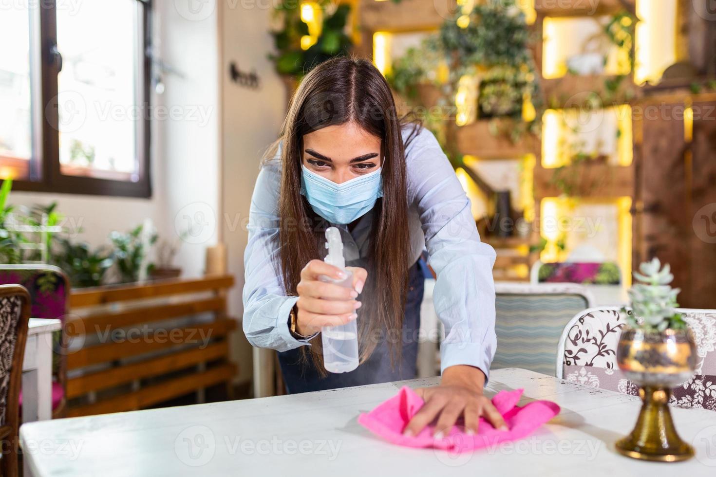 porträt einer attraktiven kellnerin, die eine gesichtsmaske trägt und den tisch vor dem willkommenen kunden mit alkohol und feuchttüchern reinigt. neue normalität mit dem hygiene-restaurantkonzept des coronavirus-ausbruchs. foto