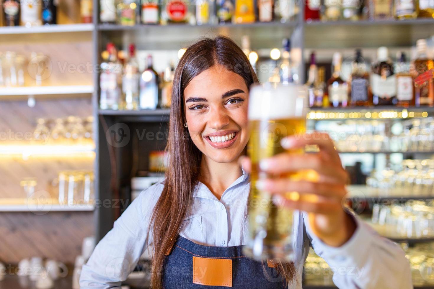 junge Frau, die Bier vom Fass serviert. lächelnde Barkeeperin, die im Pub frisches Bier aus dem Hahn in das Glas gießt. foto