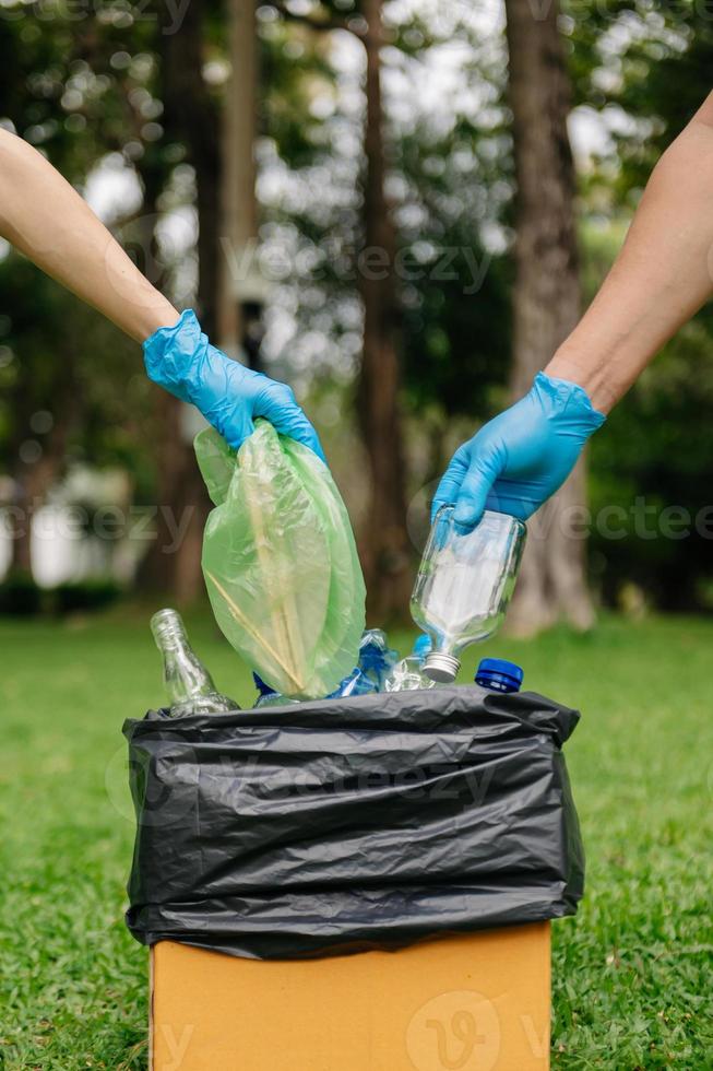 leute halten müllflasche plastik und glas in der hand und legen sie in den recyclingbeutel. reinigung, verschmutzung, ökologie und plastikkonzept. foto
