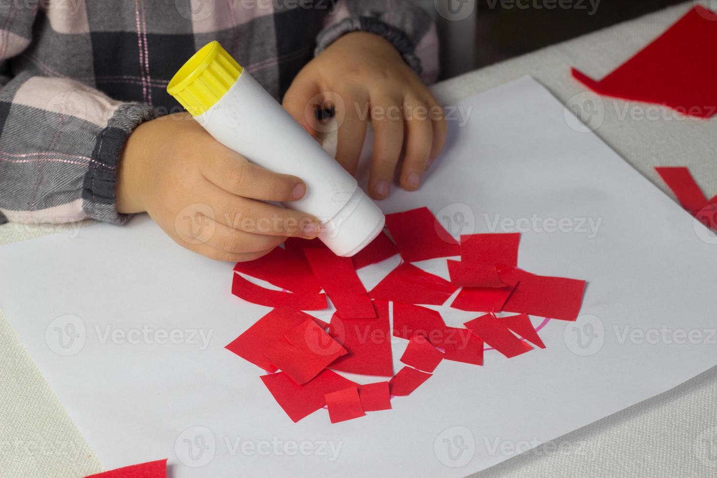 Kleines Mädchen, das rote Herzapplikationen mit Papier und Kleber auf weißem Blatt macht, Valentinstagsgrußkarte, Weihnachtsgeschenk für Muttertag, handgemachtes Kindergeschenk, Liebessymbol mit Papier, Kleinkindaktivität foto