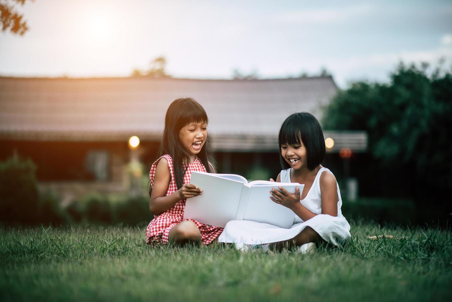 zwei kleine Mädchen im Park auf dem Rasen, die ein Buch lesen und lernen foto