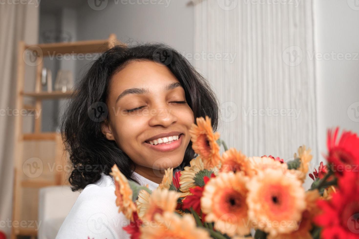 glückliches afroamerikanisches mädchen, das in die kamera lächelt und einen blumenstrauß hält. feiertagsfeierkonzept. jubiläums- oder valentinstagkonzept. foto