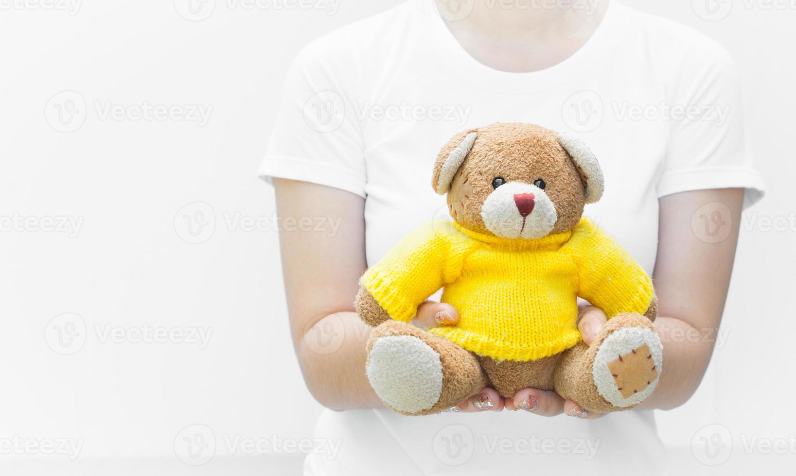 Frau, die hält und schützt, gibt einen braunen Teddybären, Spielzeug, gelbe Hemden, die auf weißem Hintergrund sitzen, Nahaufnahme, Symbol der Liebe oder Verabredung foto