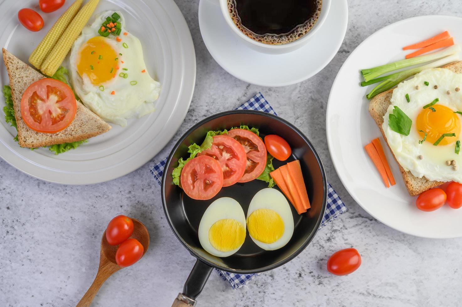 gekochte Eier, Karotten und Tomaten mit Löffel und Kaffeetasse foto