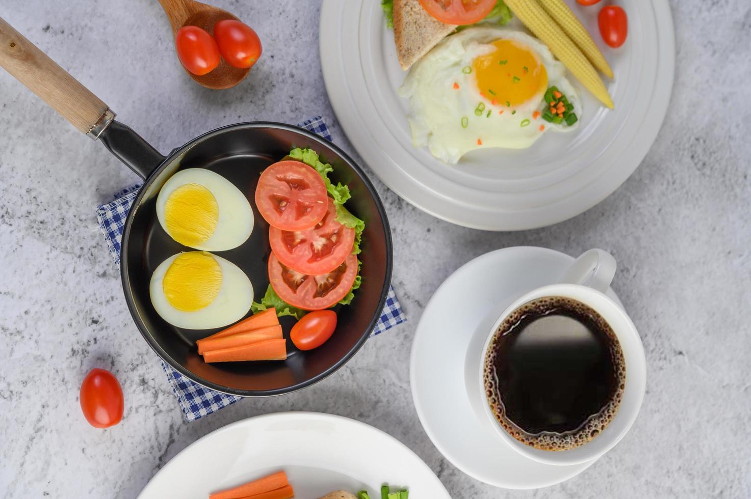 gekochte Eier, Karotten und Tomaten mit Löffel und Kaffeetasse foto