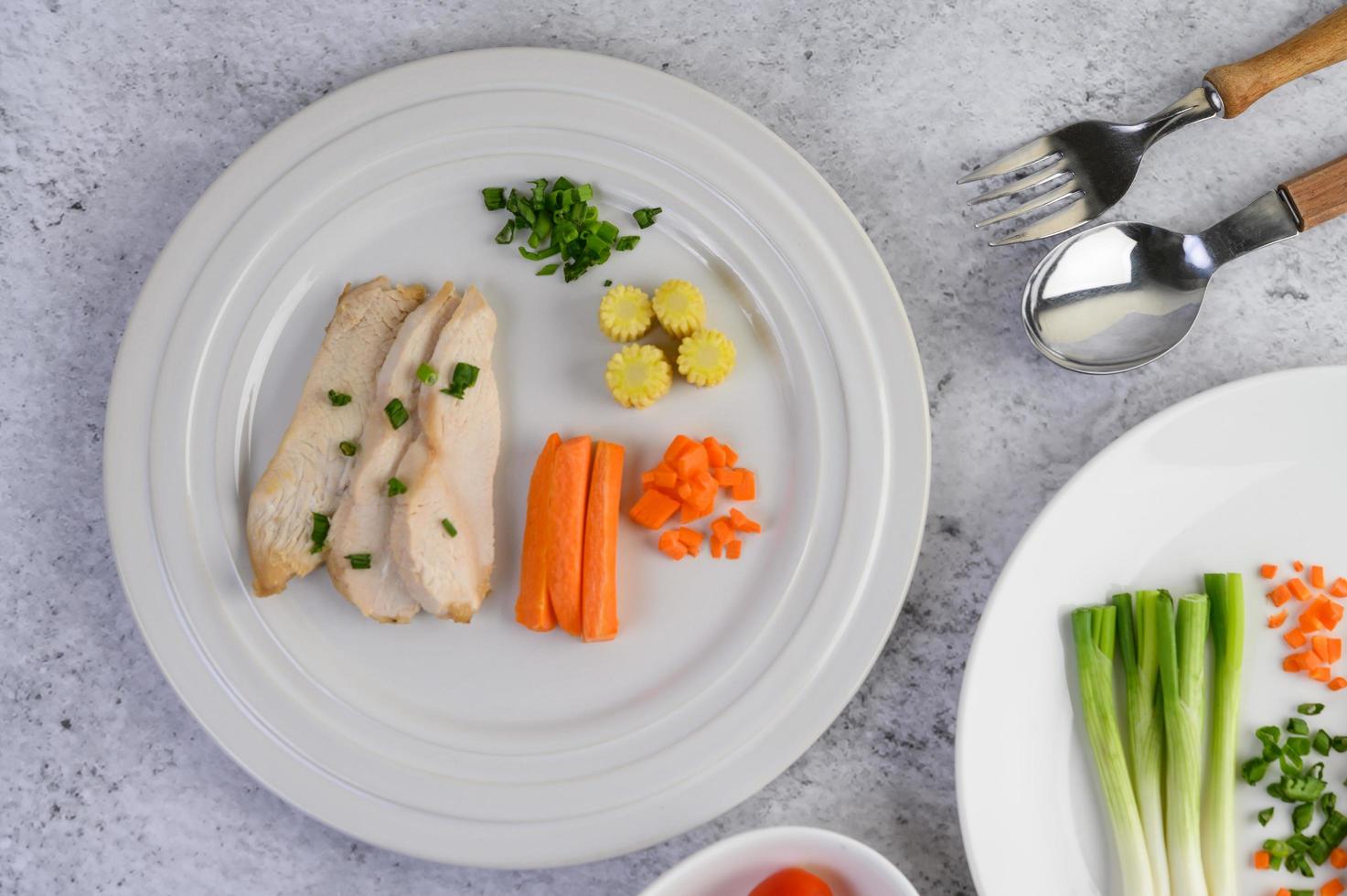 gedämpfte Hühnerbrust auf einem weißen Teller mit Frühlingszwiebeln und Karotten foto