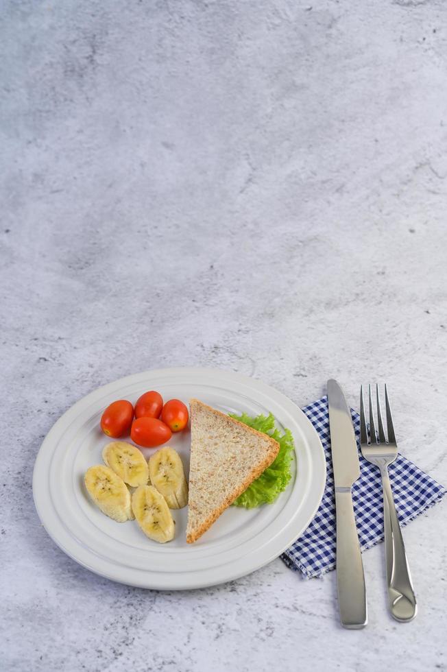 Brot mit Banane und Tomaten auf einem weißen Teller foto