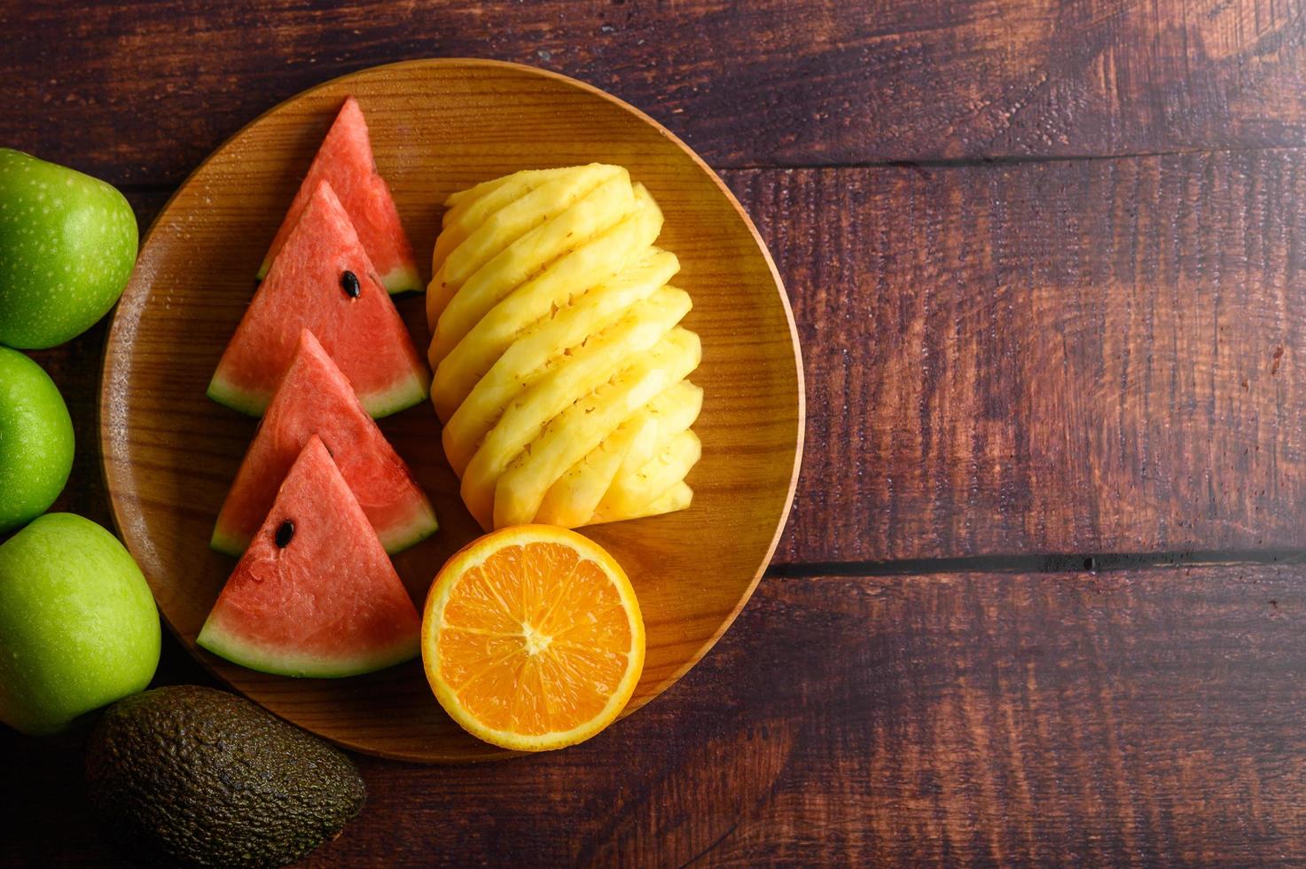 Wassermelone, Orange und Ananas auf einem Holzteller in Stücke geschnitten foto