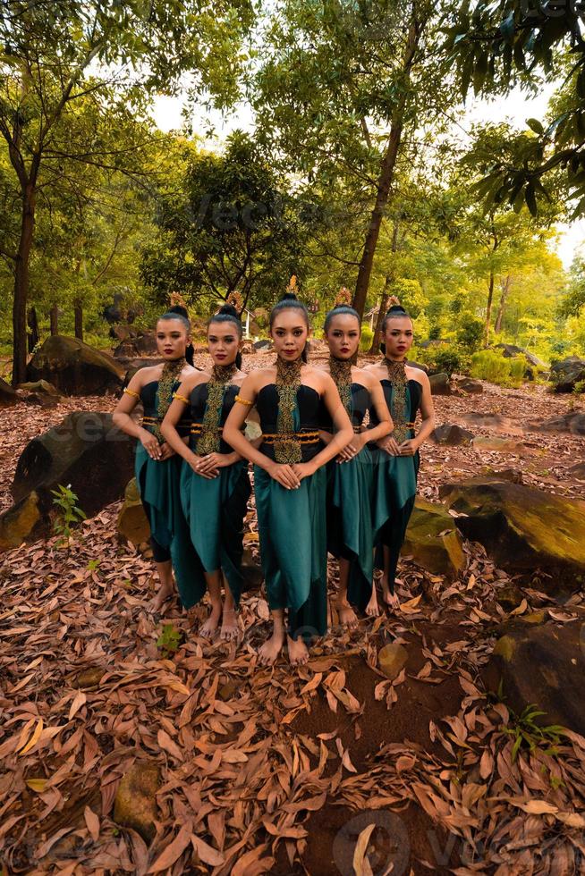 eine Weiteinstellung einer asiatischen Frau, die zusammen im Wald steht, während sie ein grünes Tanzkostüm mit abgestorbenen Blättern trägt foto