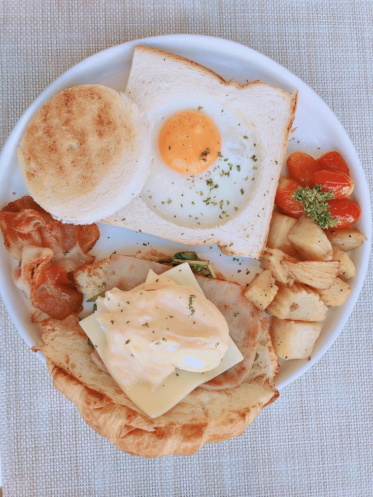 hausgemachtes Frühstück - Spiegeleier, Speck, Schinken, Tomaten, Käse, Kartoffeln und Toast, Draufsicht. foto