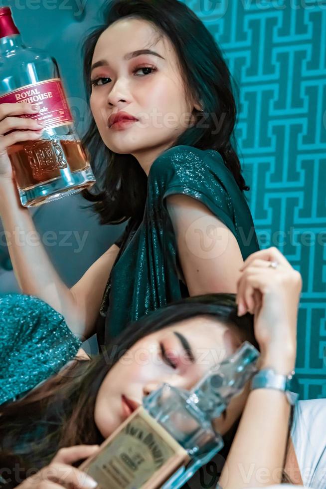 asiatische frauen, die im schlafzimmer eine alkoholflasche in der hand halten foto