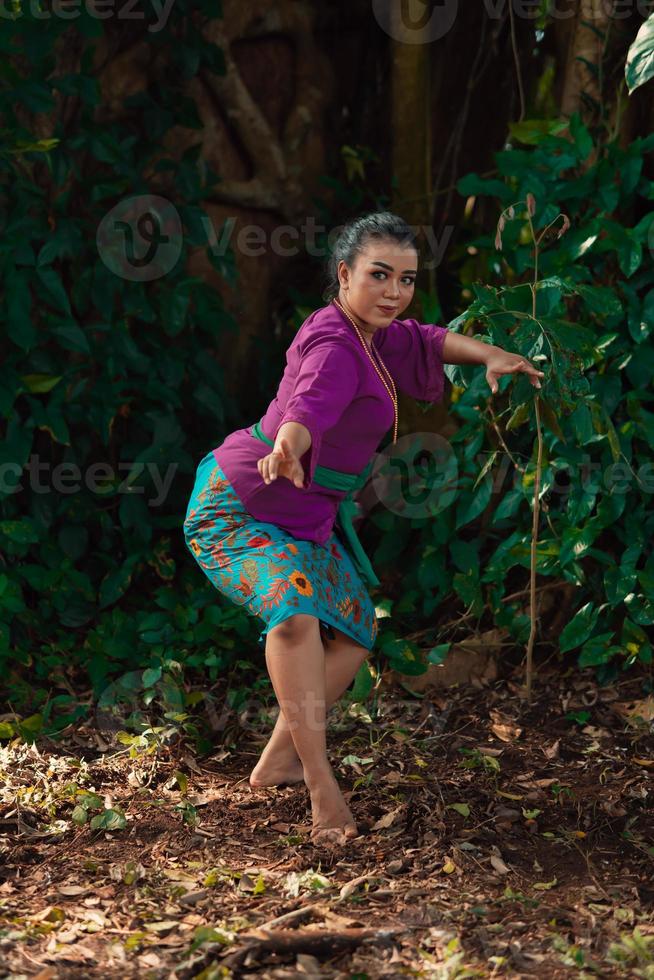 sexy sundanesische Frau mit lila Kleid tanzt vor dem großen Baum und den grünen Blättern im Hintergrund foto