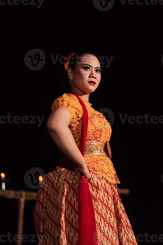 tapfere balinesische frau posiert mit einem wütenden ausdruck, während sie ein traditionelles orangefarbenes kleid und make-up trägt foto