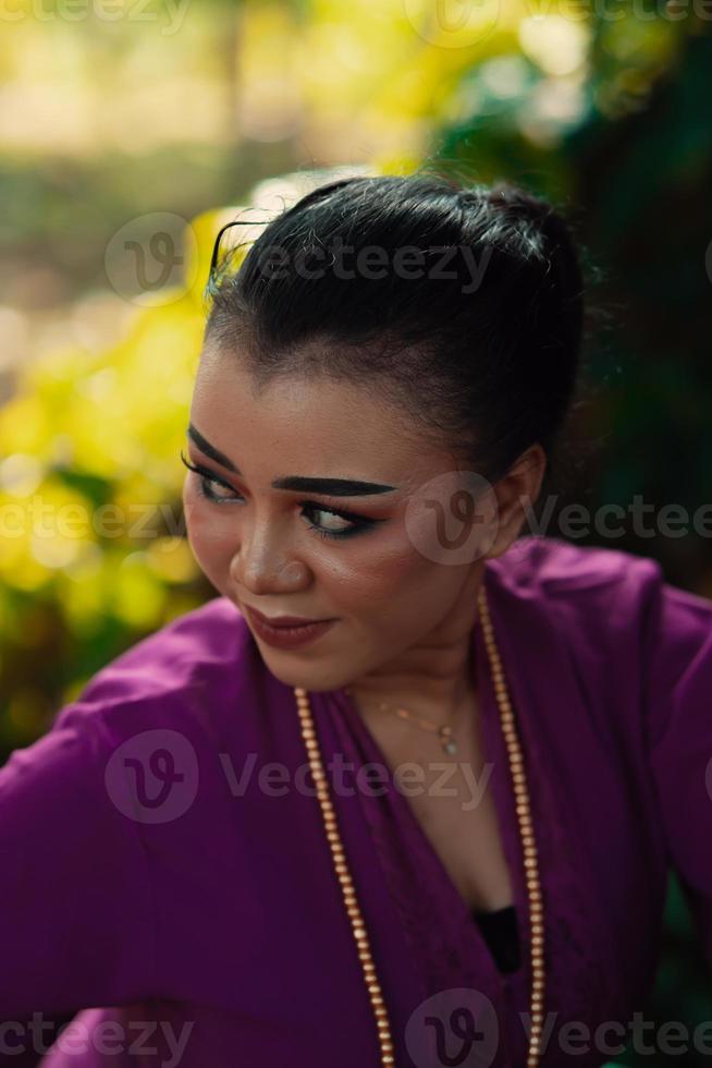 das Gesicht einer javanischen Frau mit Make-up und einem traditionellen lila Kleid namens Kebaya, während sie mit Schmuck am Hals tanzt und posiert foto